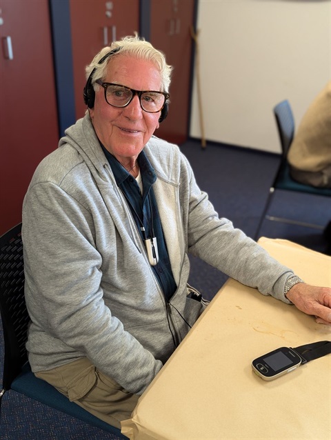 Person sitting at a table using a hearing loop, looking at the camera and smiling.