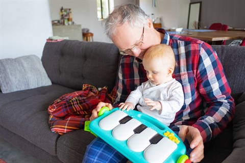 grey-haired-grandfather-sitting-couch-playing-with-baby