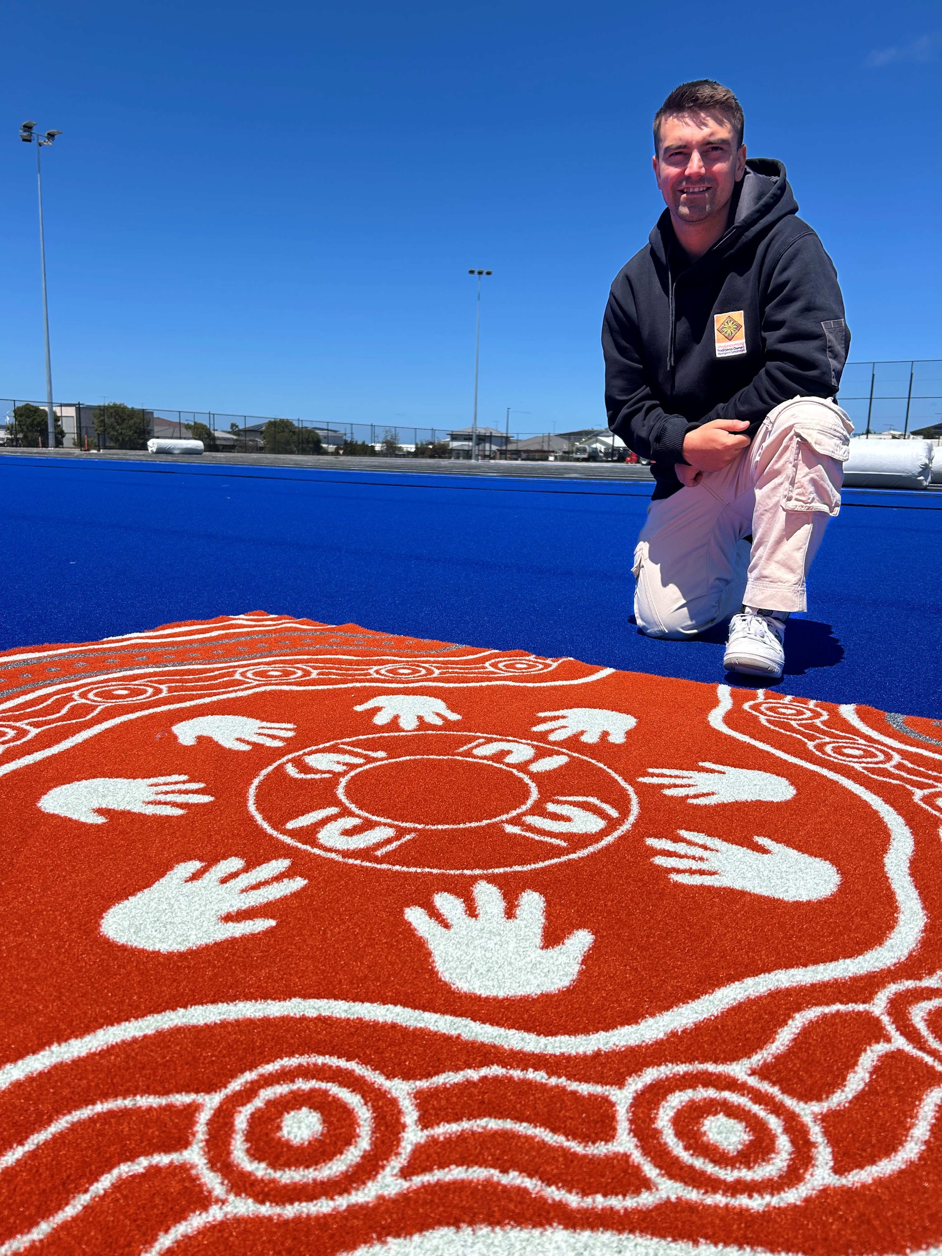 First Nations artist Billy-Jay O'Toole with his artwork, to be stitched into Banyul-Warri Fields Hockey Pitch.jpg