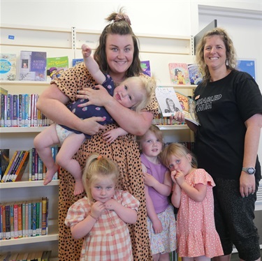 Parent with four young children standing in front of a bookshelf with Renee d'Offay at the Torquay Library.
