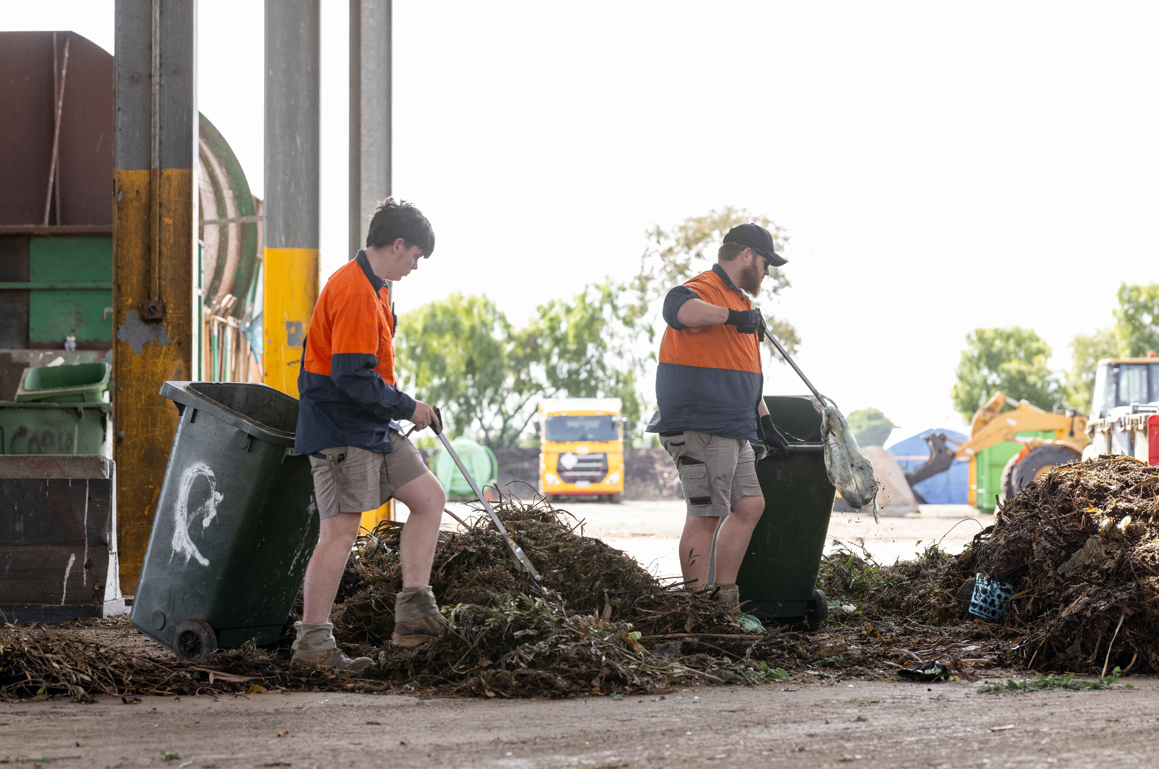 Two people in high vis using rakes on a pile of organic waste