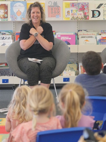 Renee d'Offay sitting on a chair signing Koala in Auslan to children at the Torquay Library